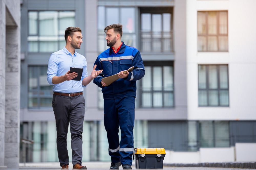 Gestionnaire et technicien de maintenance échangeant sur le terrain devant un immeuble